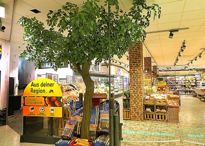 Kunstbaum, 320 cm hoch, im Eingangsbereich eines Lebensmittelmarktes.